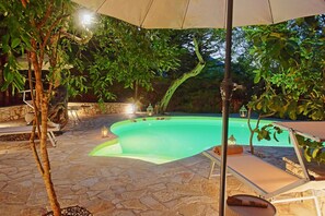 Una piscina esterna con pavimento in pietra, circondata da alberi e un muro in pietra.