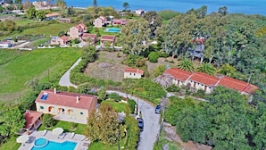 An aerial view of a coastal residential area with houses, a swimming pool, and a road.