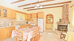 A kitchen with wooden cabinets, a dining table with a checkered tablecloth, a built-in oven, and a tiled floor.