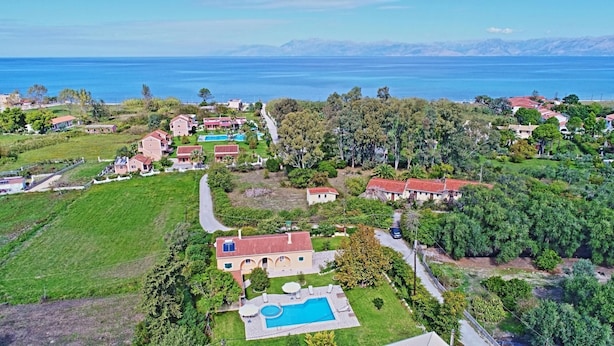 An aerial view of a coastal residential area with houses, a swimming pool, and a clear view of the sea.
