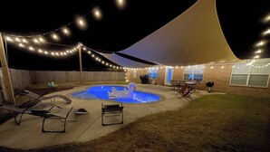 An outdoor pool area with a tent, string lights, and lounge chairs.