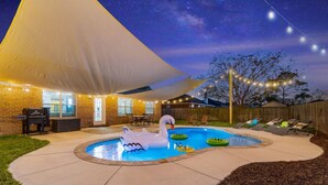 A backyard with a swimming pool, a swan inflatable, and a barbecue grill.