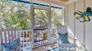 A covered porch with white railings, two patterned chairs, and a decorative octopus wall art piece. - Chic + Modern BHI Retreat, Both Clubs, 3 Golf Carts, 5 Porches w/Great Views (Bald Head Island)
