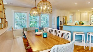 A modern kitchen with white cabinetry, a wooden dining table, and a bar area. - Chic + Modern BHI Retreat, Both Clubs, 3 Golf Carts, 5 Porches w/Great Views (Bald Head Island)