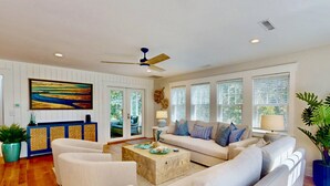 A spacious living room with a beige sofa set, a coffee table, and a large painting on the wall. - Chic + Modern BHI Retreat, Both Clubs, 3 Golf Carts, 5 Porches w/Great Views (Bald Head Island)
