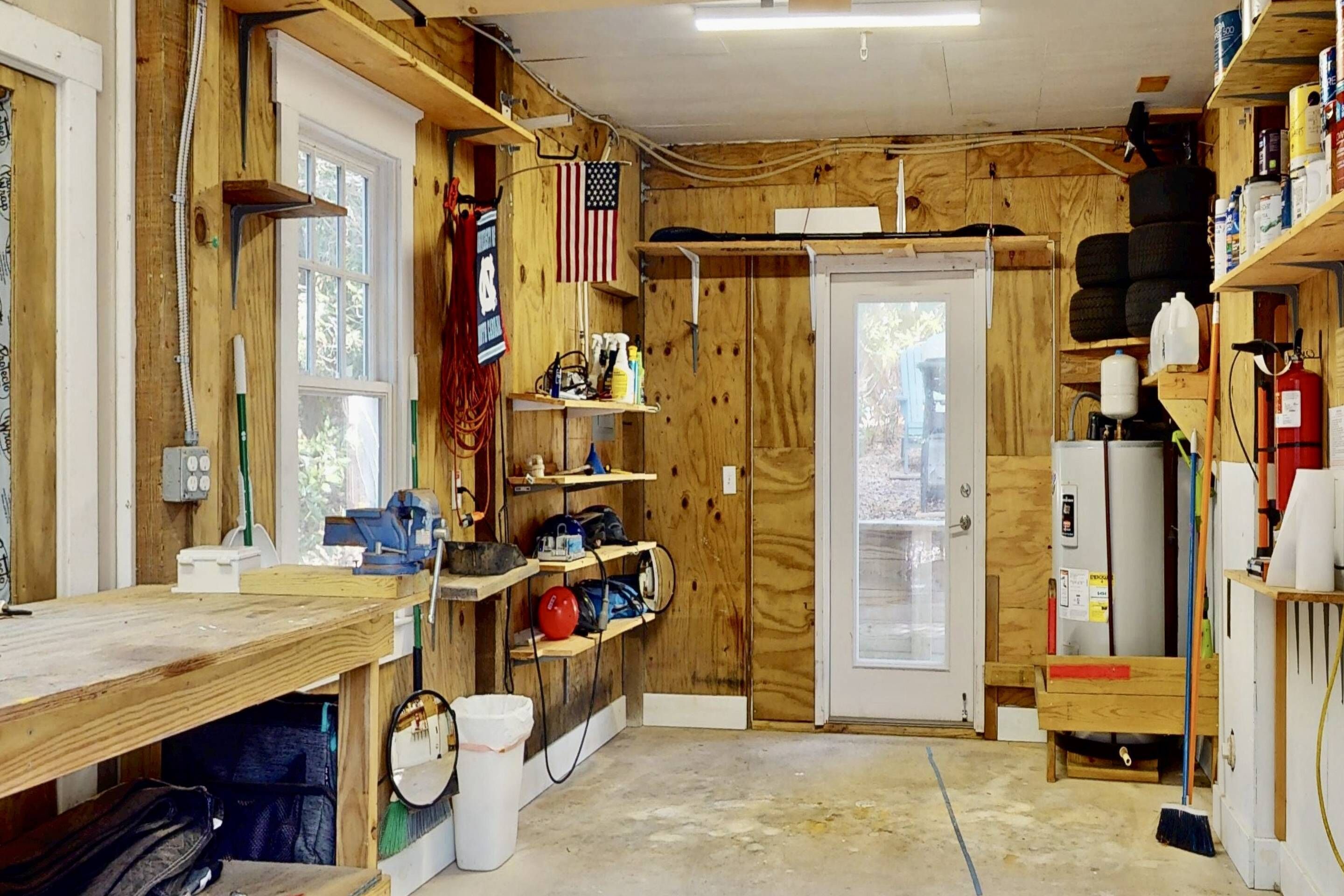 A workshop with wooden walls, shelves with tools, a workbench, and a door with a window.