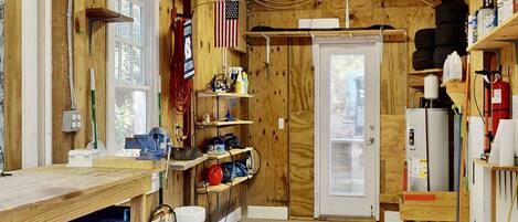 A workshop with wooden walls, shelves with tools, a workbench, and a door with a window.