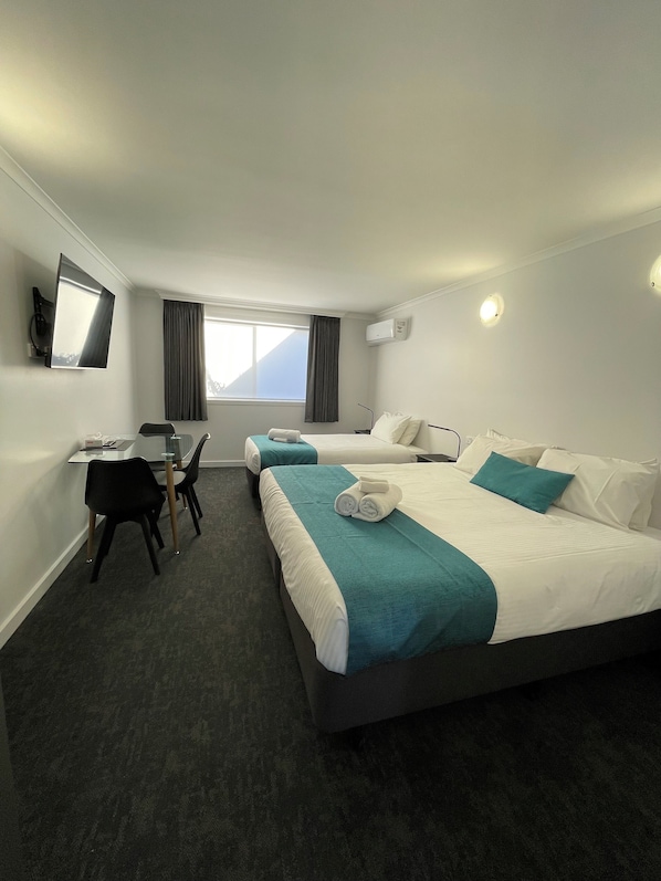 A hotel room with two beds, a desk, chairs, a TV, and a window with curtains.
