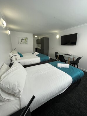A hotel room with two beds, a desk, a TV, and a bathroom visible through an open door.