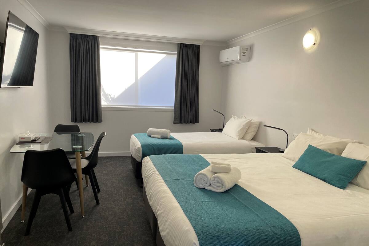 A hotel room with two beds, a desk, a chair, and a window with curtains.