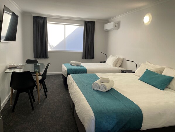 Habitación de hotel con dos camas, un escritorio, una silla y una ventana con cortinas.