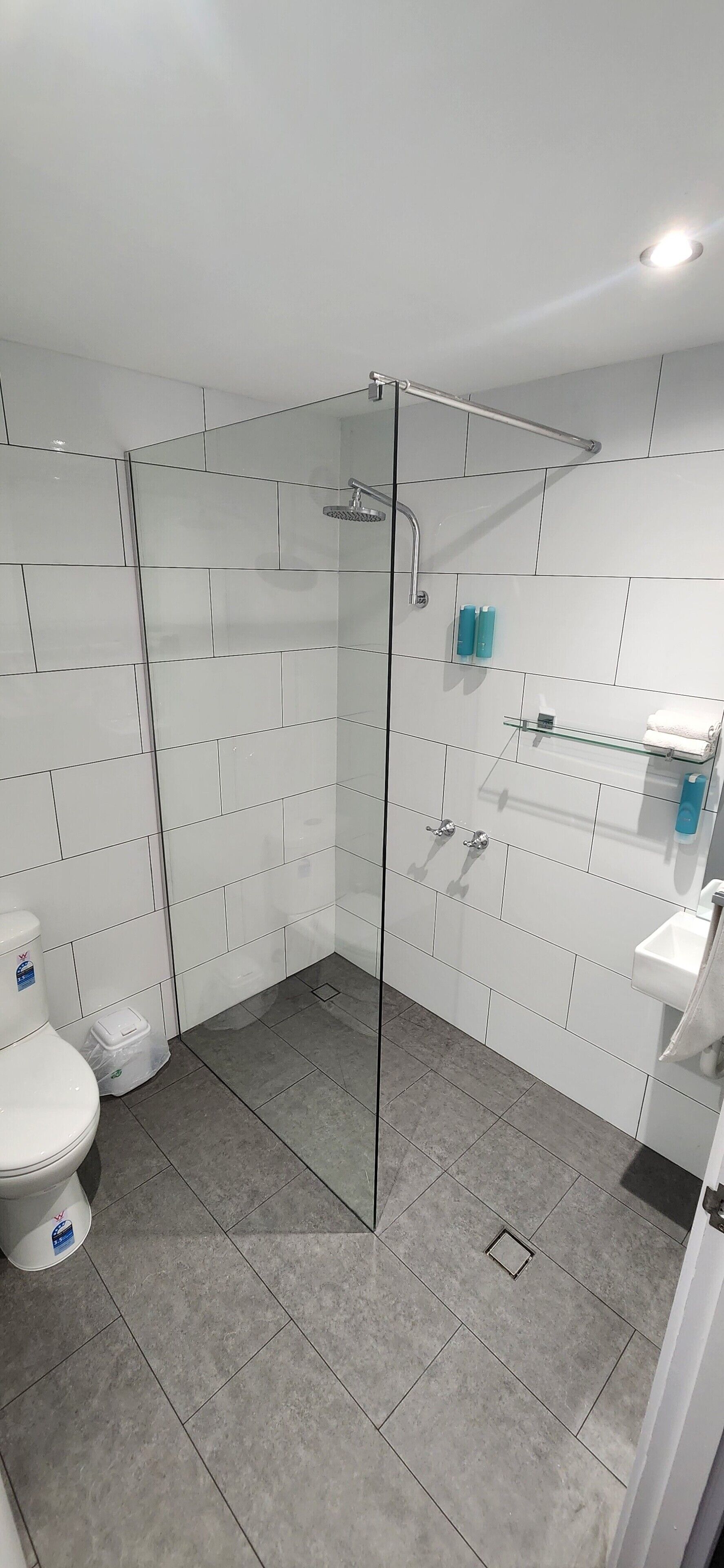 A modern bathroom with a glass-enclosed shower, white tiled walls, a white toilet, and a sink with a mirror.