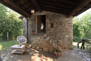 A rustic stone building with a wooden balcony, a wicker chair, and potted plants.