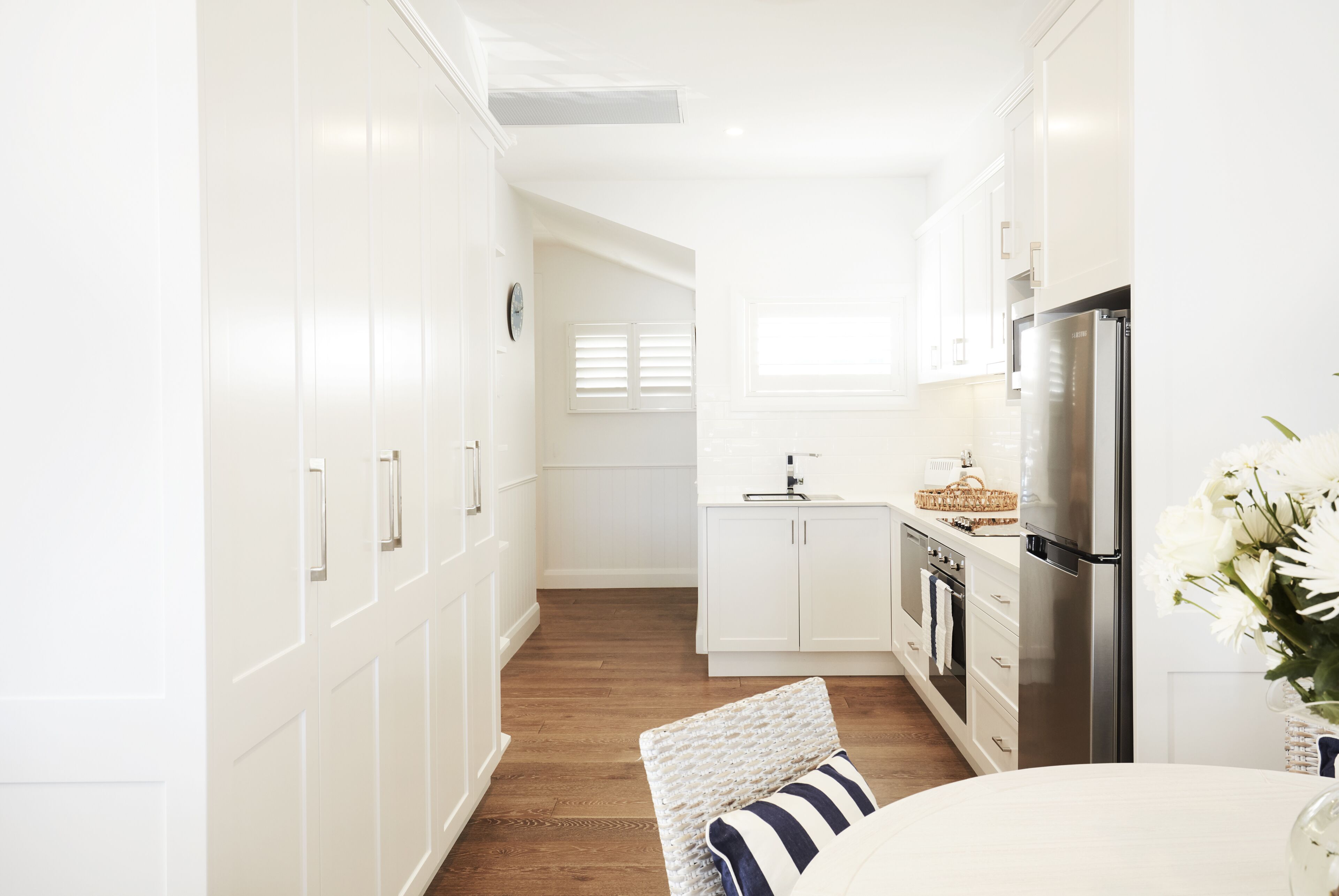 A modern kitchen with white cabinetry, a stainless steel refrigerator, and a wooden floor.