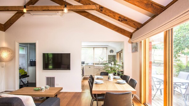 Un comedor amplio con una mesa y sillas de madera, un televisor montado en la pared, y un ventanal que ofrece vistas al exterior.