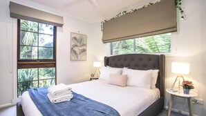 Una cama bien tendida con un edredón azul, dos lámparas de noche y una ventana con vistas a zonas verdes.