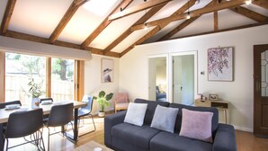 Una sala de estar moderna con un sofá gris oscuro, una mesa de comedor de madera y sillas. Hay un ventanal que proporciona luz natural y vistas al exterior.