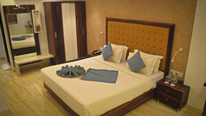 Una cama bien hecha con almohadas y una toalla, una mesita de noche con un teléfono y botellas de agua, y un espejo con una repisa encima.