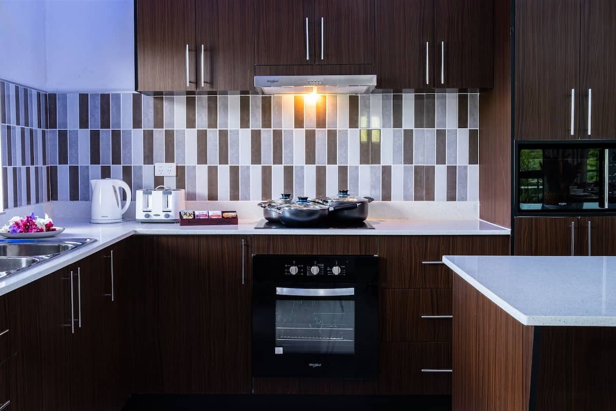 Une cuisine moderne avec des meubles de couleur bois foncé, un évier en acier inoxydable, un four encastré et un four à micro-ondes.