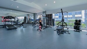 Un gimnasio moderno con diversos equipos de ejercicio, ventanas amplias y un reloj visible en la pared.