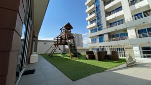 Un patio de juegos en la azotea con una estructura de madera, césped artificial y mobiliario de mimbre.
