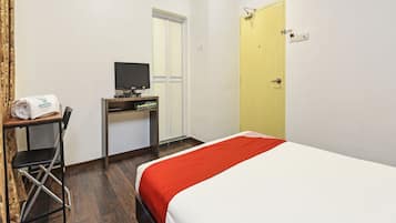 A hotel room with a bed, a desk with a television, a chair, an air conditioning unit, and a door.