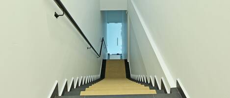 Una escalera con peldaños alternados en color negro y beige, balaustres blancos y barandilla negra.
