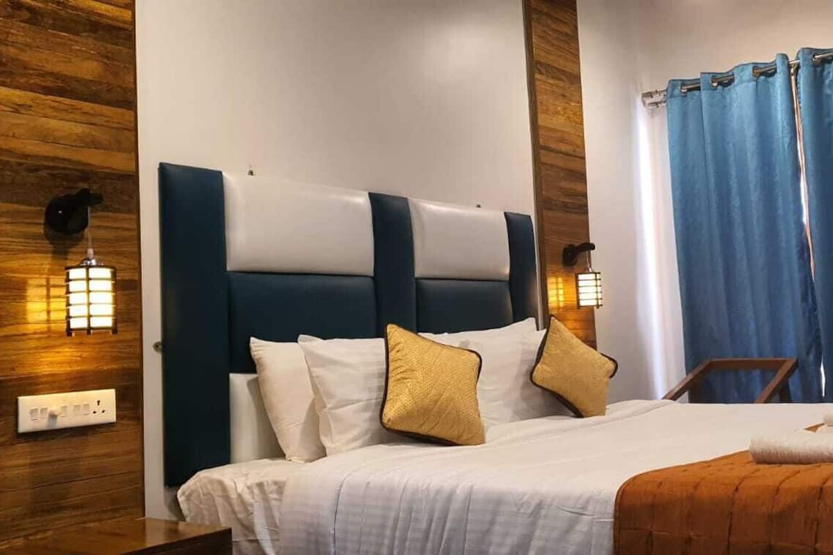 A hotel room with a large bed, two bedside tables, a wooden headboard, and a window with blue curtains.