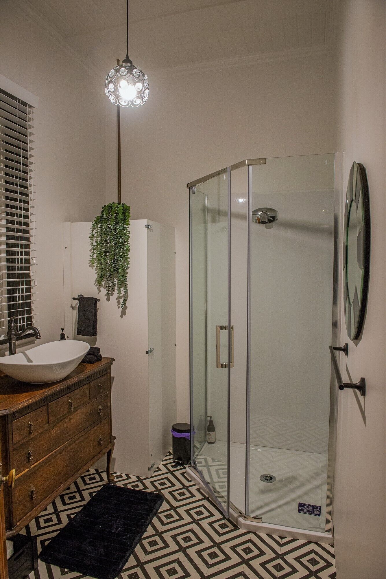 Een badkamer met een douchecabine van glas, een houten wastafelmeubel met een wastafel en een hangplant.