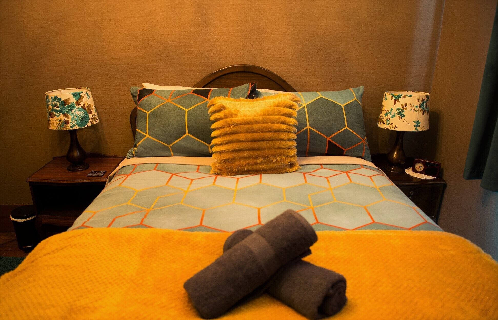 Un lit bien fait, recouvert d’une couvre-lit à motifs géométriques, avec deux oreillers assortis et une pile de serviettes pliées posée sur le lit.