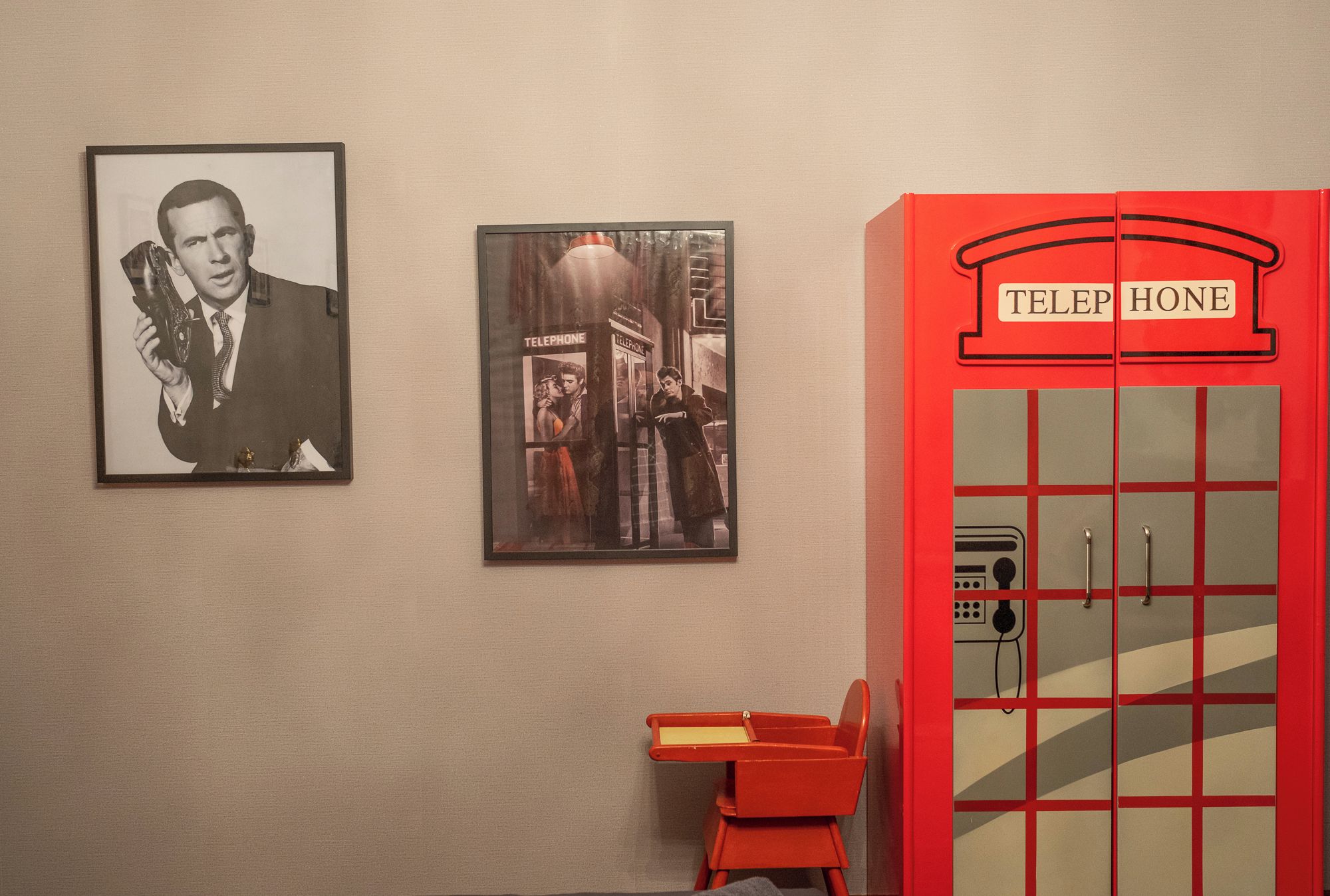 Una parete con due quadri appesi e un armadietto rosso simile a una cabina telefonica.