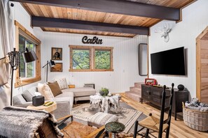 A cozy cabin interior with a couch, a coffee table, a TV, and a mounted deer head.