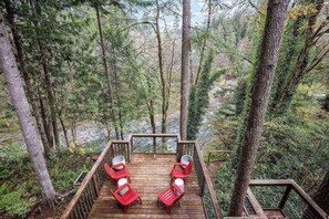 A wooden deck with red chairs and a table, surrounded by trees.