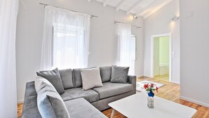 A modern living room with a grey sofa, white curtains, and a white coffee table with a vase. - Villa Regina in Kentroma (Corfu)