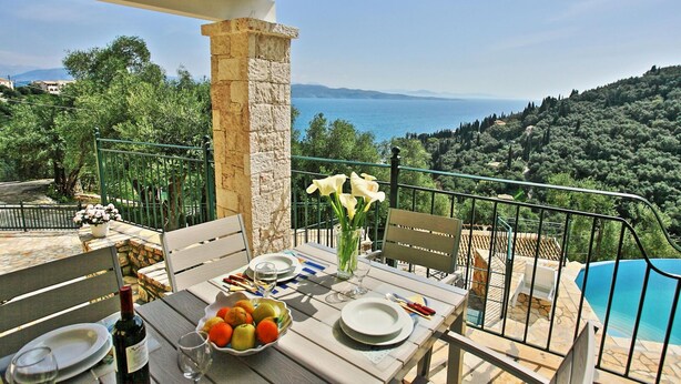 A terrace with a table set for dining, overlooking a scenic view of the sea and hills. - Villa Regina in Kentroma (Corfu)