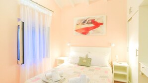 A bedroom with a bed, two bedside tables, a nightstand, a window with sheer curtains, and a painting on the wall. - Villa Regina in Kentroma (Corfu)