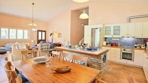 Een ruime keuken met een centraal eiland, een eethoek met een houten tafel, en een zithoek met een bank en stoelen.