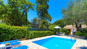 Ein Swimmingpool mit blauem Wasser, umrandet von Steinplatten, beschattet von einem weißen Sonnenschirm.