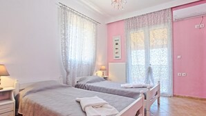 A bedroom with two beds, a radiator, a window with patterned curtains, and a wall-mounted air conditioning unit. - Sunset House in Sidari (Corfu)