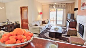 A living room with a sofa, a coffee table, a TV, and a fireplace. There is a door leading to another room and a window with curtains. - Sunset House in Sidari (Corfu)