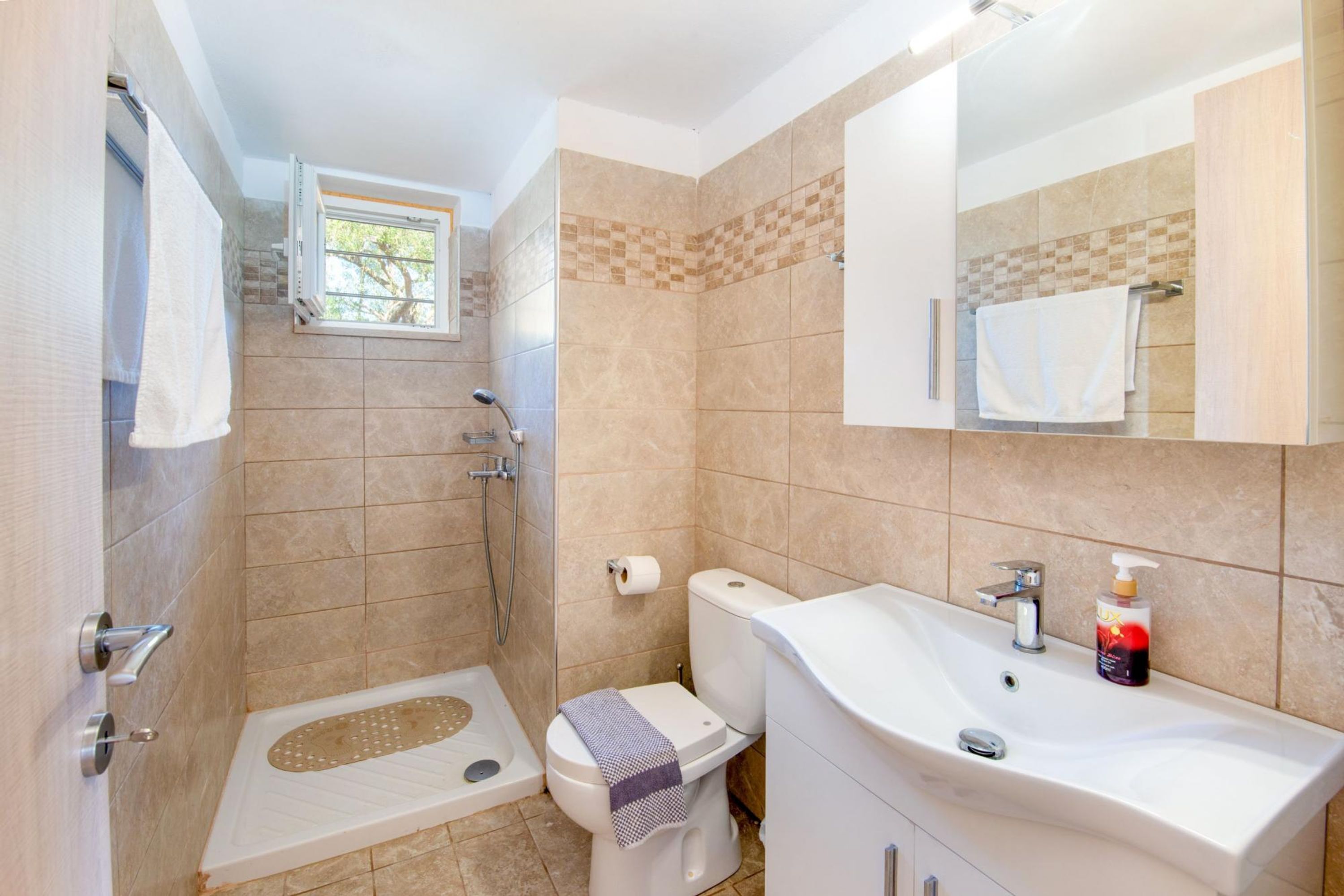 A bathroom with a shower, toilet, sink, and a window.