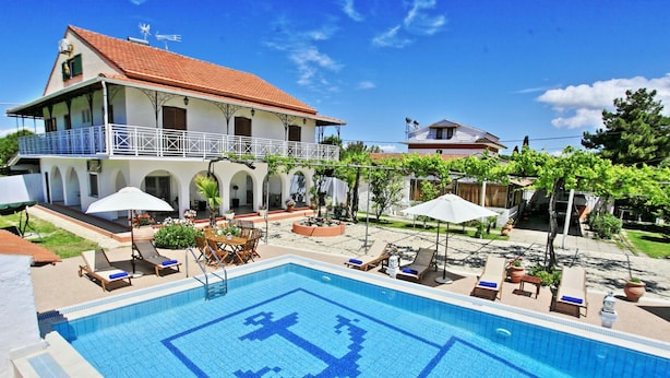 Ein Pool mit geometrischem Muster, ein zweistöckiges Gebäude mit Balkon und Sitzgelegenheiten mit Sonnenschirmen.