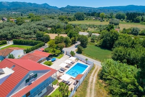 Área residencial com piscina, edifícios com telhados vermelhos e uma estrada serpenteando pela paisagem.