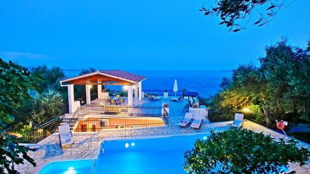 A poolside area with a building, lounge chairs, and a view of the sea. - Villa Alexandros in Nisaki (Corfu)