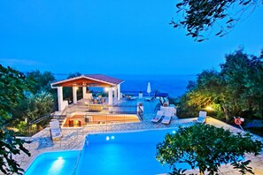 A poolside area with a building, lounge chairs, and a view of the sea. - Villa Alexandros in Nisaki (Corfu)