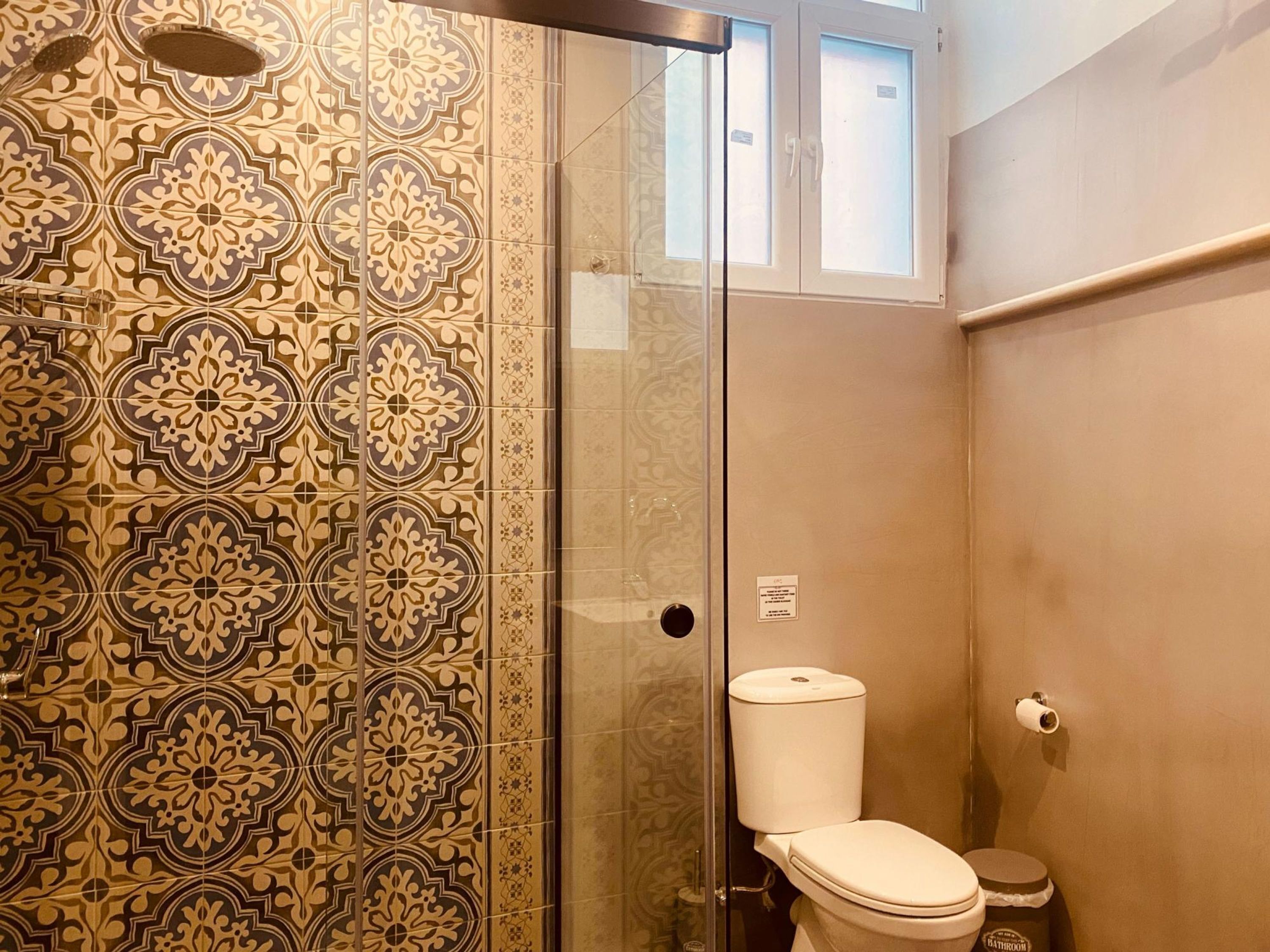 A bathroom with patterned tiles, a toilet, a shower enclosure, and a glass door.