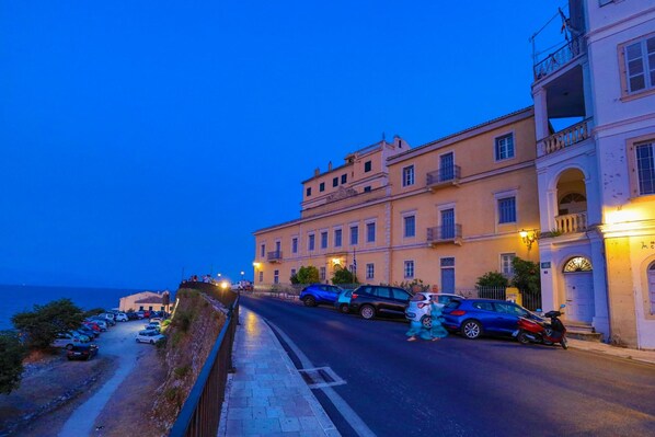 A coastal street with parked cars and a building with balconies. - Mouragia House in Kerkira (Corfu)
