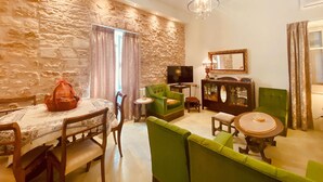 A living room with a stone wall, a television, a green sofa, and a dining table with chairs. - Mouragia House in Kerkira (Corfu)