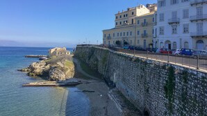 A coastal town with a stone wall, clear blue sea, and buildings along the waterfront. - Mouragia House in Kerkira (Corfu)