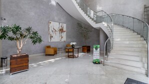 Eine geräumige Lobby mit Marmorboden, einer modernen Treppe und einem großen abstrakten Gemälde an der Wand.